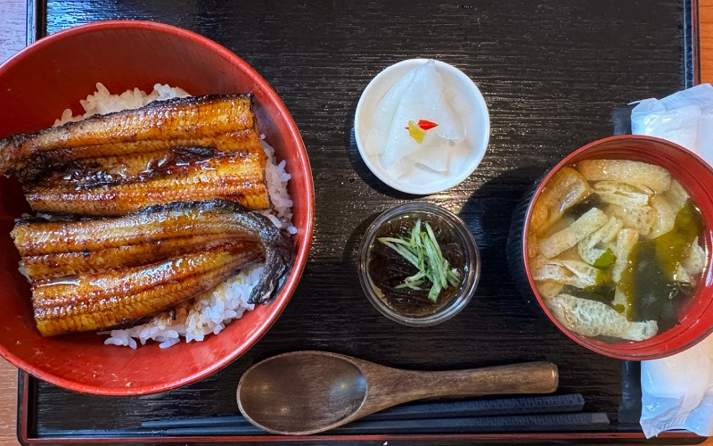 黑色托盤上俯視鰻魚丼套餐,附漬物、小菜與味噌湯