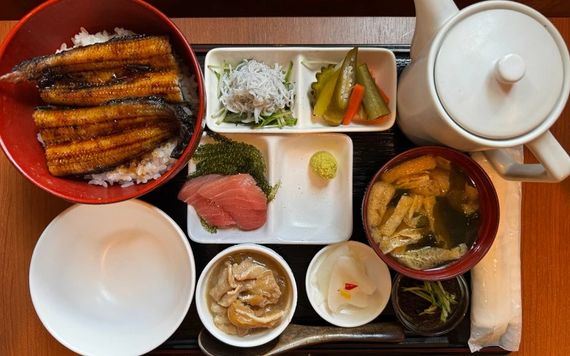 鰻魚丼套餐俯視圖,附鮪魚生魚片、漬物、配菜與白色茶壺
