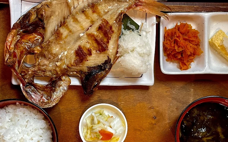 整尾大型烤魚盛於白盤,附白飯、醃紅蘿蔔、玉子燒與味噌湯