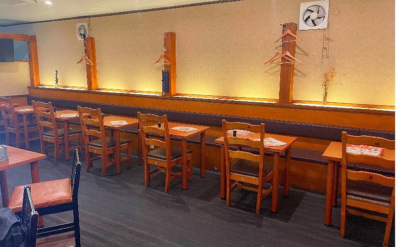 餐廳內部,木製桌椅沿牆排列,座位上方掛有衣架,暖色燈光