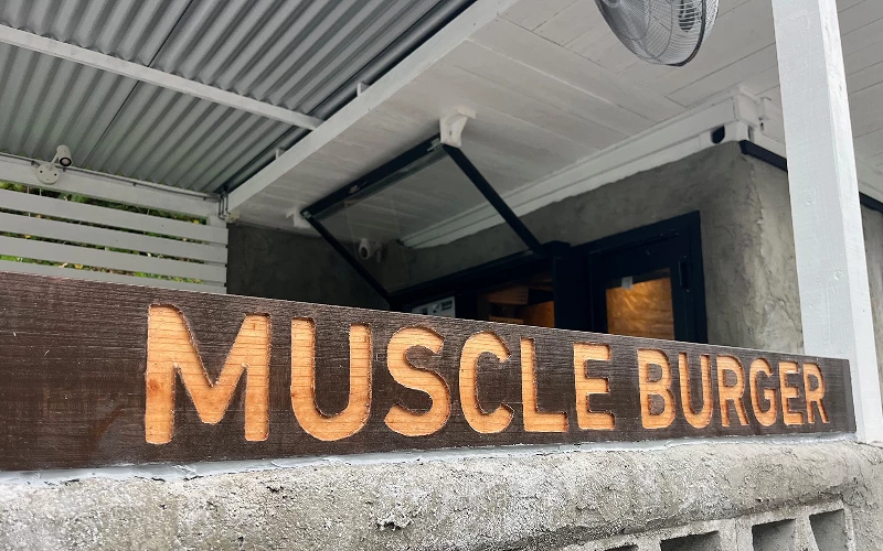 深木色店頭招牌雕刻「MUSCLE BURGER」字樣,位於店門廊下