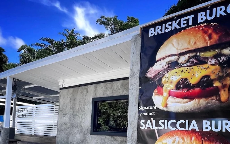 店外牆面貼有「BRISKET BURGER」與「SALSICCIA BURGER」英文海報,白色屋頂建築