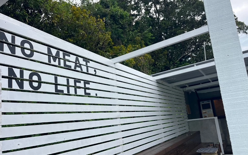 白色木條圍欄上漆印「NO MEAT, NO LIFE.」字樣,背景為店門入口