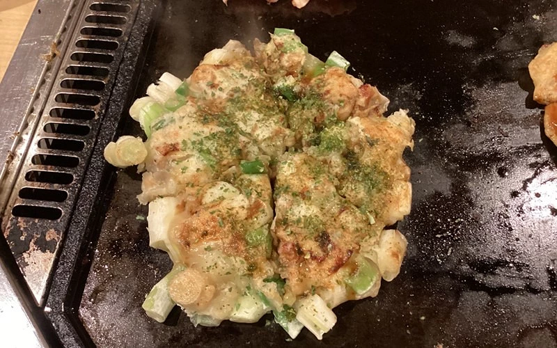 鐵板上煎烤帶蔥花的大阪燒,表面撒有青海苔