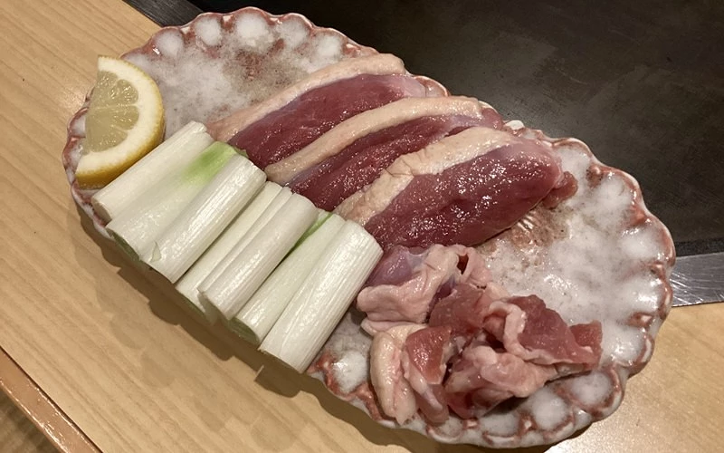 花形盤盛生鴨肉片、長蔥段與小塊內臟,旁附檸檬切片