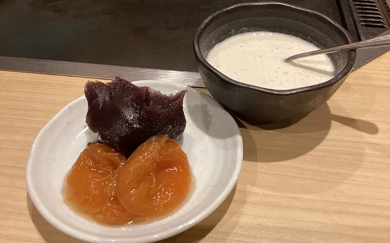 白色小碟盛紅豆與橙色蜜漬果,旁附鐵碗盛白色甘酒