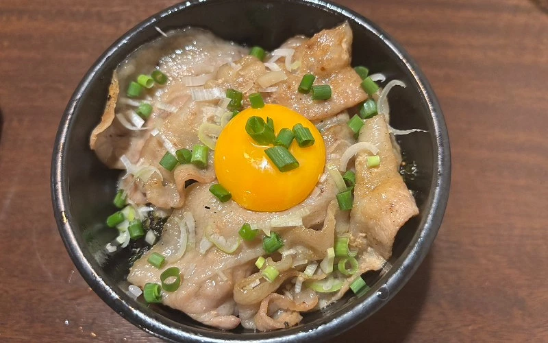 黑碗盛豬肉丼,中央放生蛋黃並撒蔥花