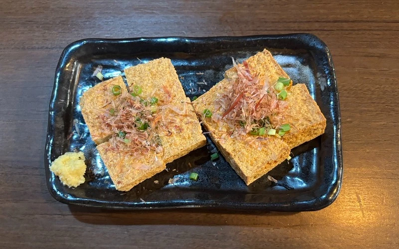 黑盤盛煎豆腐,鋪柴魚片與蔥花,旁附薑泥