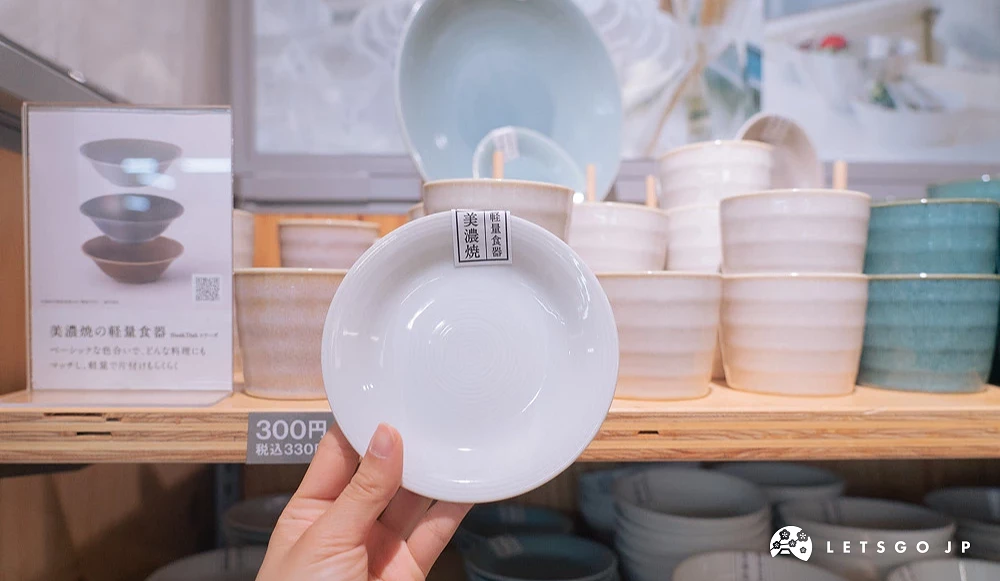 手持 Standard Products 美濃燒白色輕量餐盤,後方陳列多款不同顏色與尺寸的美濃燒餐具