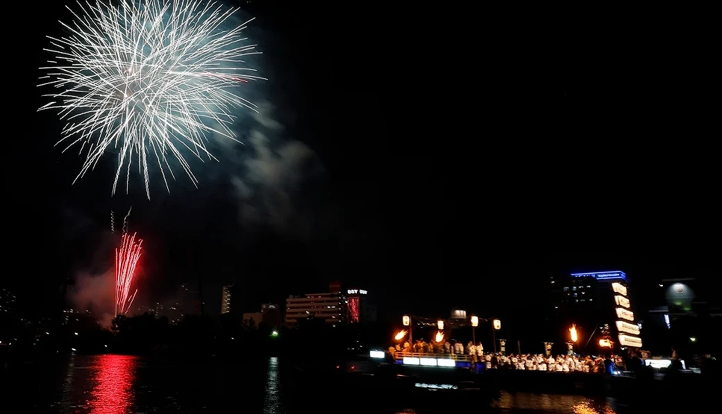 天神祭奉納煙火於大阪大川上空綻放,船渡御船隊點燃篝火巡行,煙火與燈火倒映在河面上