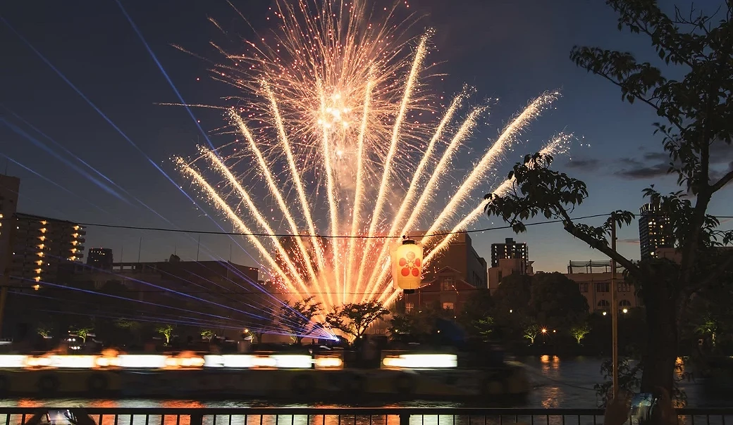 天神祭奉納煙火在大阪大川沿岸綻放,船渡御船隊行經河面,提燈、雷射光與煙火交織成夏祭夜景