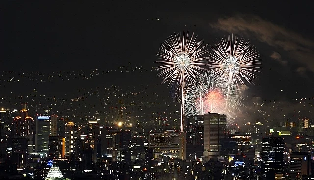 大阪市區夜景中綻放的天神祭奉納煙火,遠處可見大阪城與高樓群燈光交織的夏夜景色