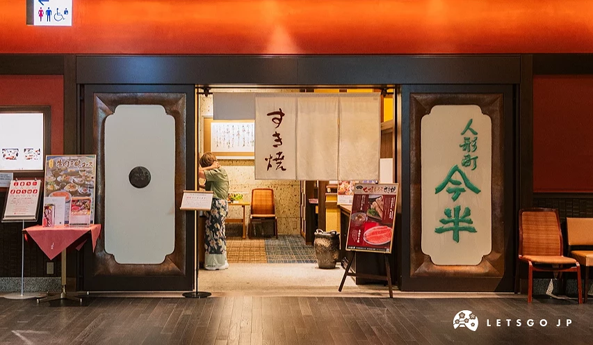 寫著「壽喜燒」日文字樣的布簾掛在店鋪門口上,右邊的牆壁上寫的「人形町今半」