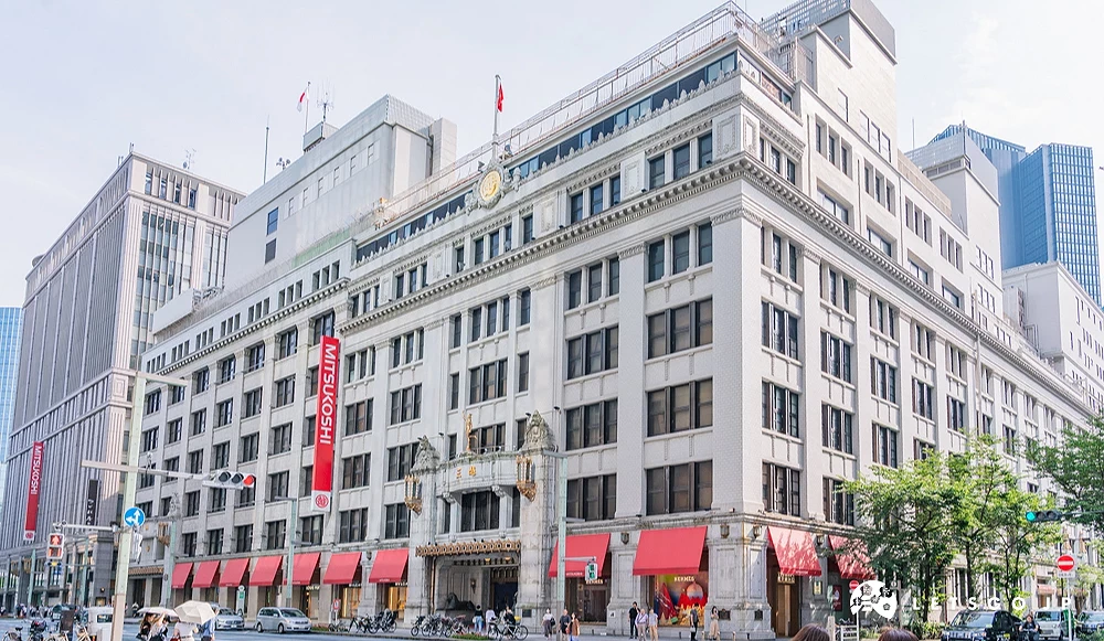 一棟六七層樓高建築,一樓的店鋪上面有紅色屋簷