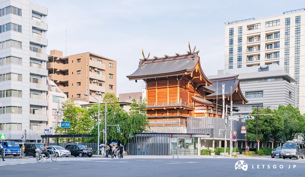 一座金色的寺廟在中間,左右有石燈和石頭道路,後面是高樓大廈