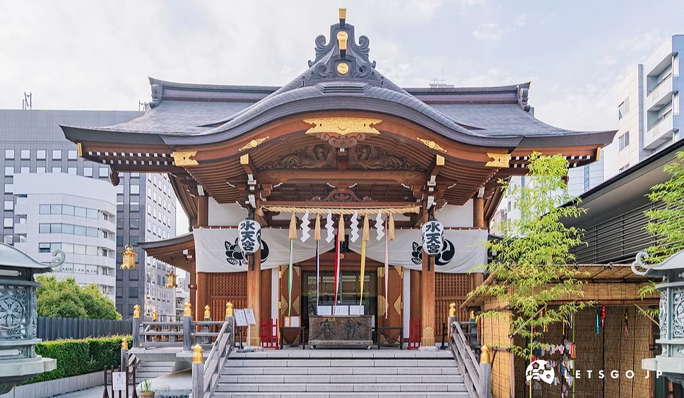 一座金色的寺廟在中間,左右有石燈和石頭道路,後面是高樓大廈