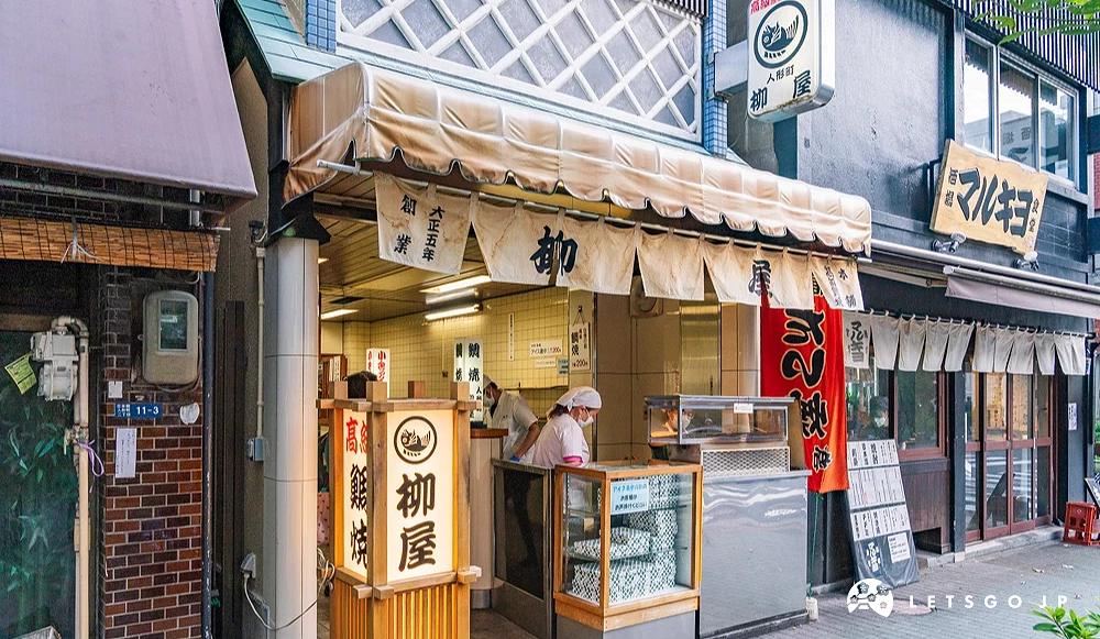 掛著白色寫著「柳屋」的布簾,有一位廚師在店門口櫃檯後,左邊有一個寫的柳屋的日式燈籠