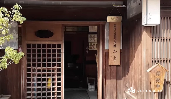 傳統木造建築立面,深褐木窗與格柵門扇古樸,招牌與盆栽點綴,日式古街風情
