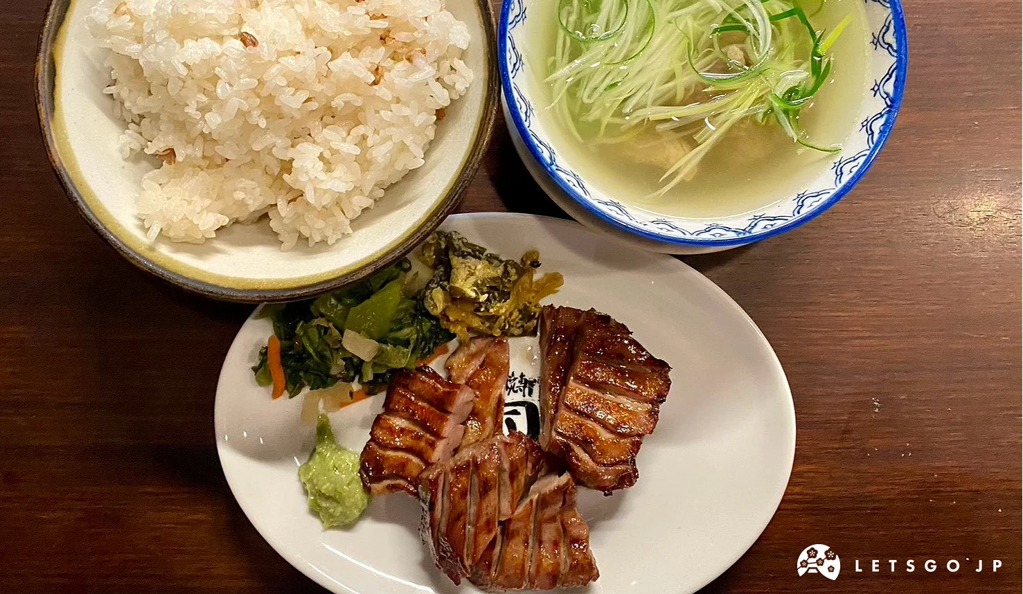 白色盤中裝有厚切烤肉片,搭配一碗白飯、綠色蔬菜與清湯
