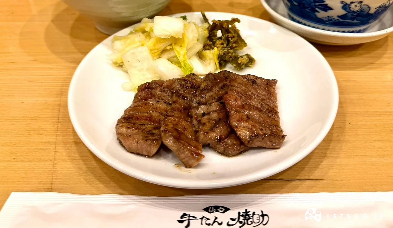 白色長盤裝有四塊烤肉與醃菜,旁邊擺放麥飯、清湯與封套筷子
