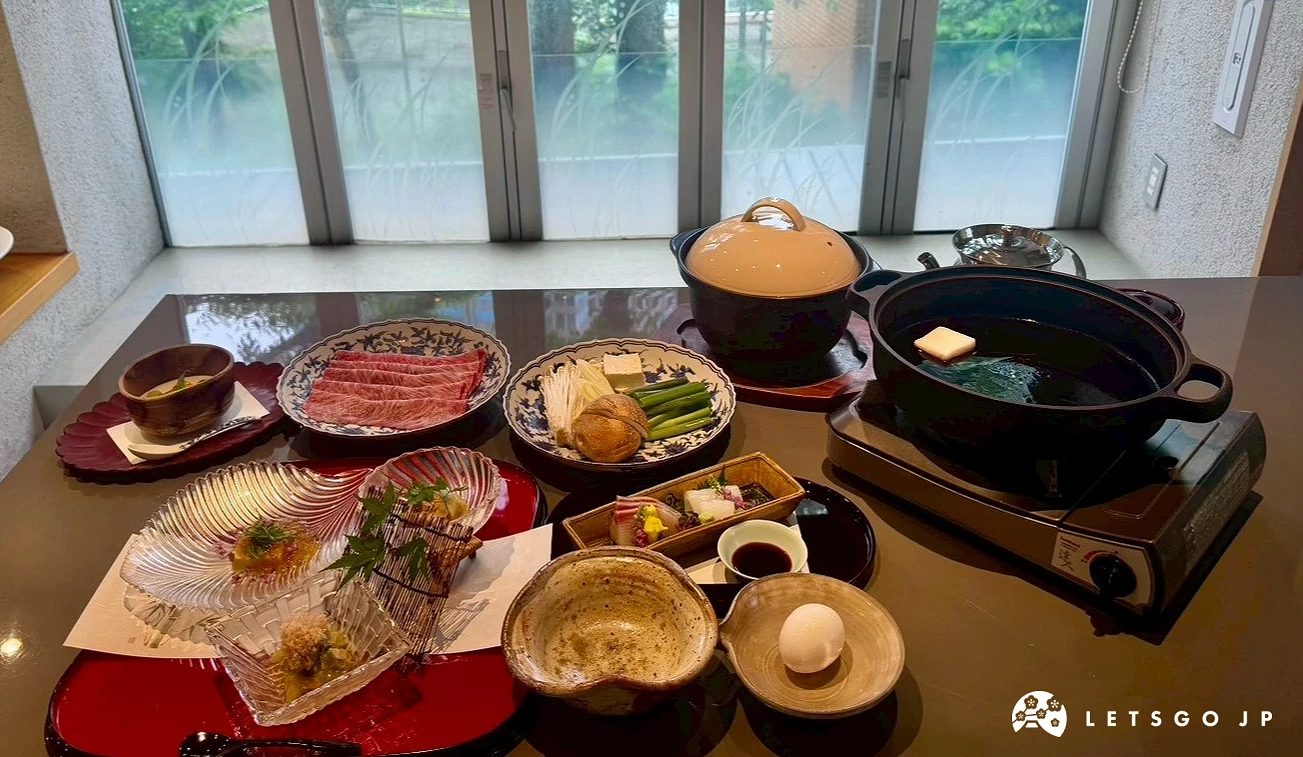靠窗餐桌上擺放著壽喜燒鑄鐵鍋、新鮮和牛肉片、生雞蛋與綜合生魚片。