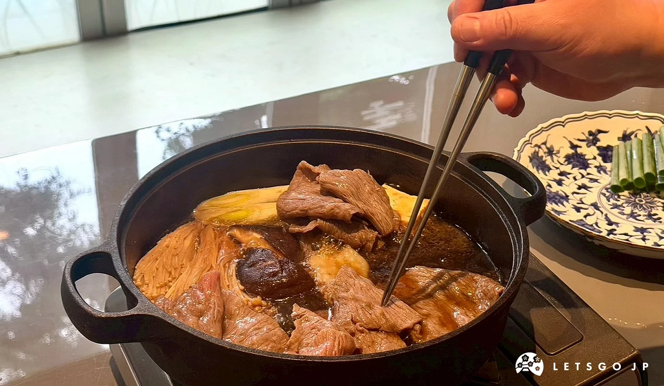 主廚手持雙筷,在桌邊的鑄鐵火鍋內翻煮壽喜燒牛肉片與大蔥。