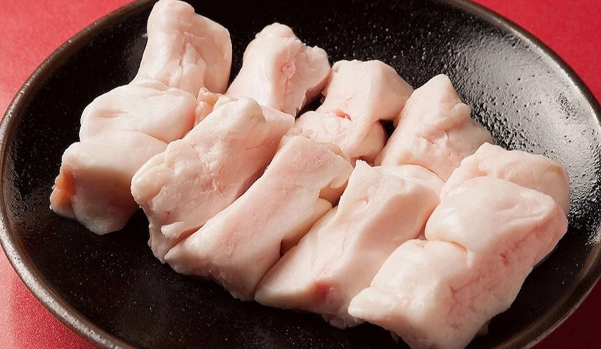 黑色陶碗盛裝白色牛小腸,肉質鮮嫩分明,紅色背景映襯日式燒肉食材。