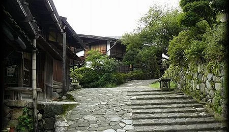 一個石板坡道路,左側有房子,右側有綠色樹木。