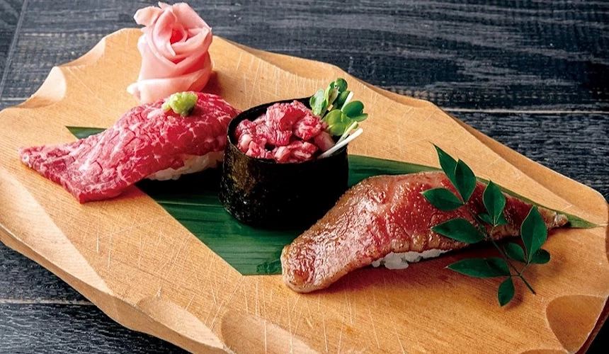 木製餐盤盛裝紅肉片、肉塊與黑碗丁寧,粉紅肉玫瑰與綠葉裝飾,日式和牛握壽司精美。