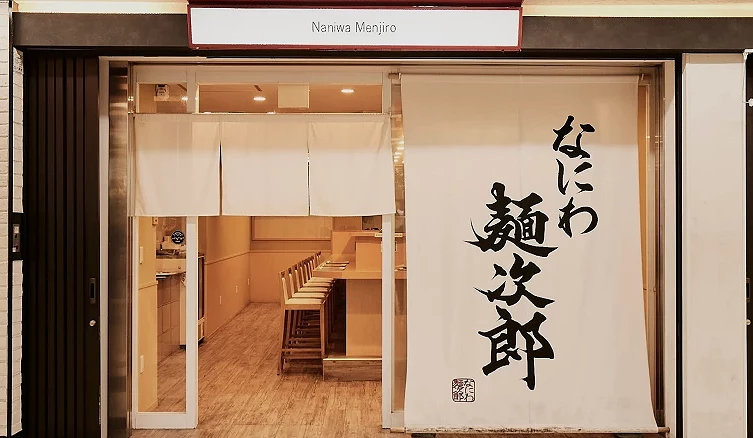拉麵店門口,右邊掛著一個白色簾子寫著「なにわ麺次郎 」