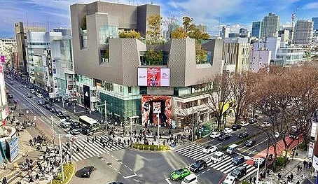 十字交叉的馬路,上面有車子跟行人,旁邊有一排樹跟百貨公司。