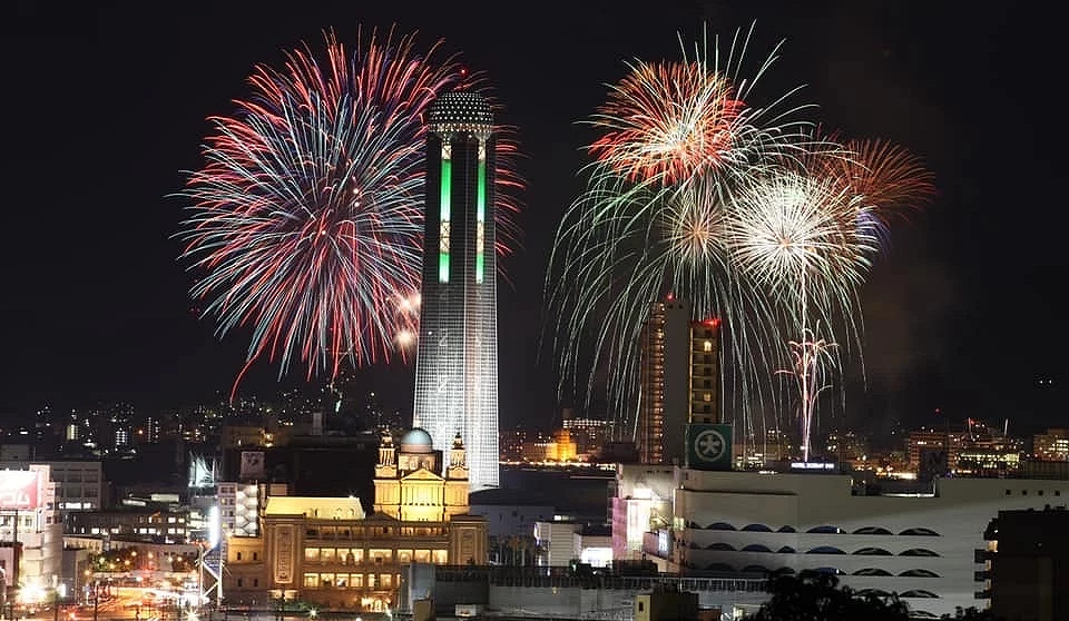 城市夜景與高聳塔樓建築,背景空中綻放著五彩繽紛的璀璨煙火