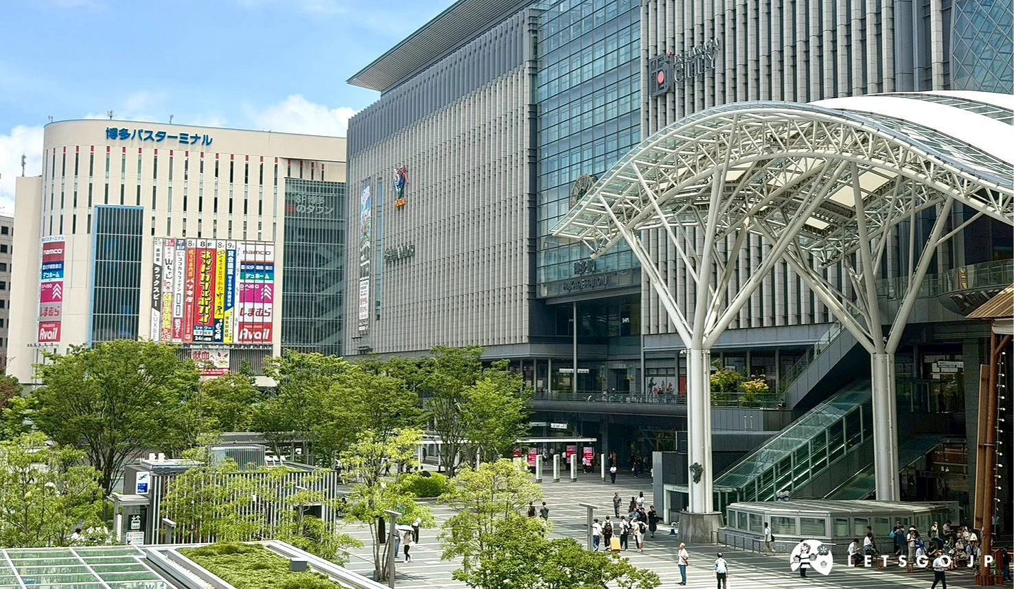藍天白雲下,博多車站現代化的鋼骨玻璃大樓外觀與前方廣場街景。