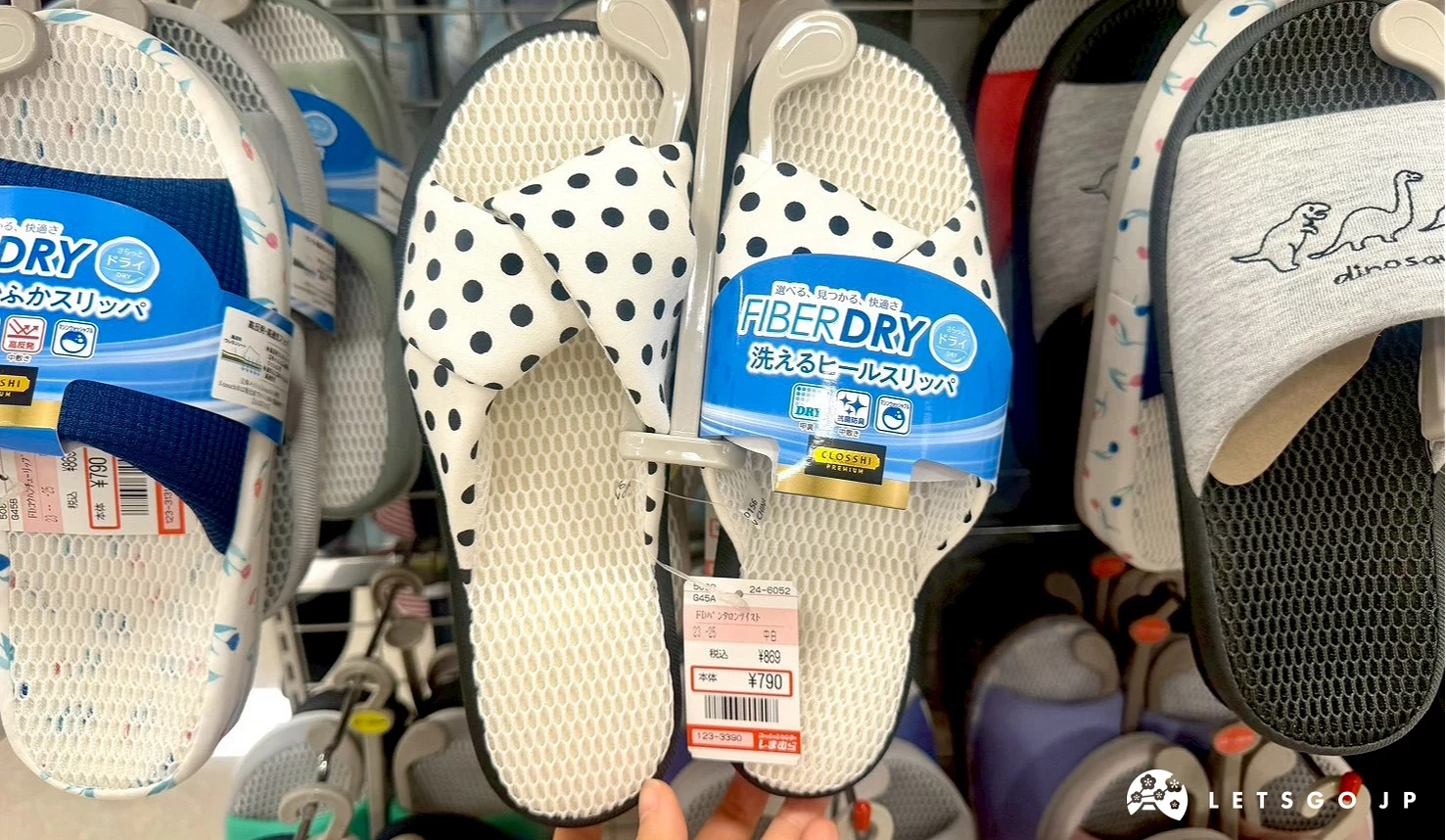 一隻手拿起展示的一雙藍白點點、印有「FIBER DRY」涼感功能標籤的女性室內防滑拖鞋。