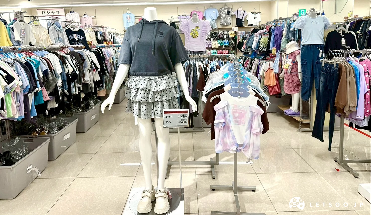 穿著灰色連帽上衣與印花短裙的少女風人型模特兒,後方有各種童裝商品。