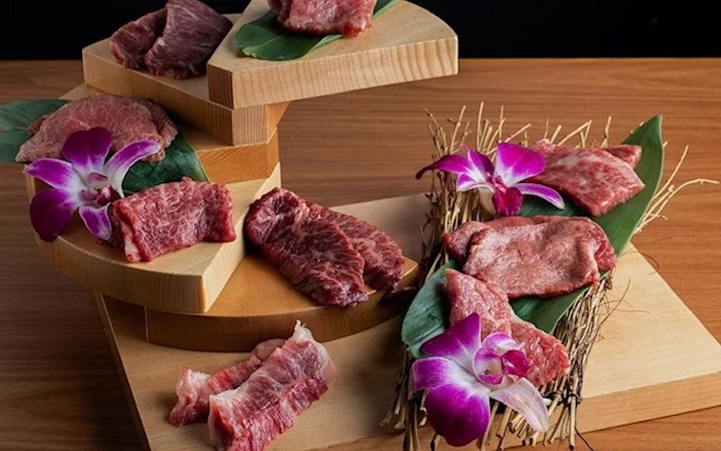 多種生和牛肉片分層擺放於木製階梯台上，以蘭花與竹草裝飾