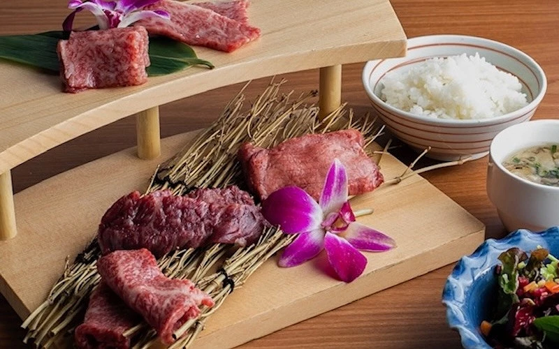 木製台上陳列多塊生和牛肉，旁附白飯與湯，點綴蘭花裝飾