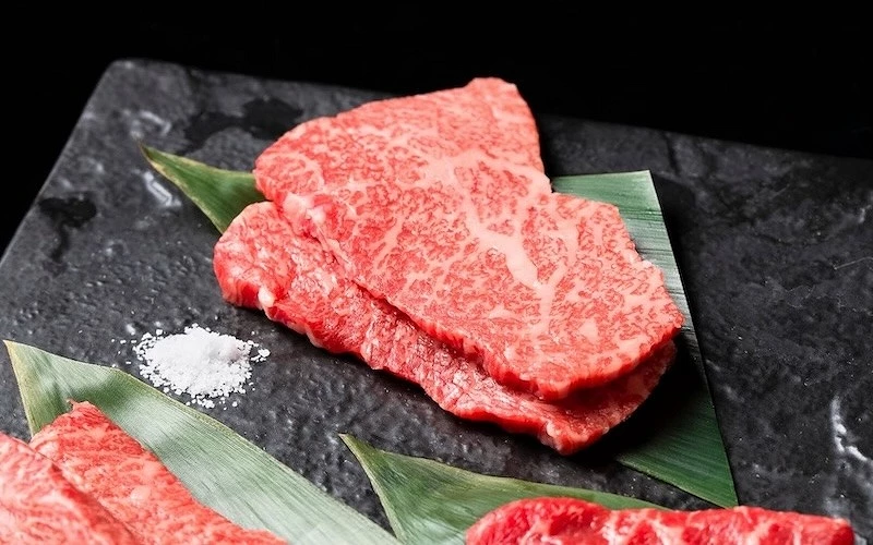 黑色石板上疊放兩片大理石油花生和牛，旁附岩鹽，置於葉片上