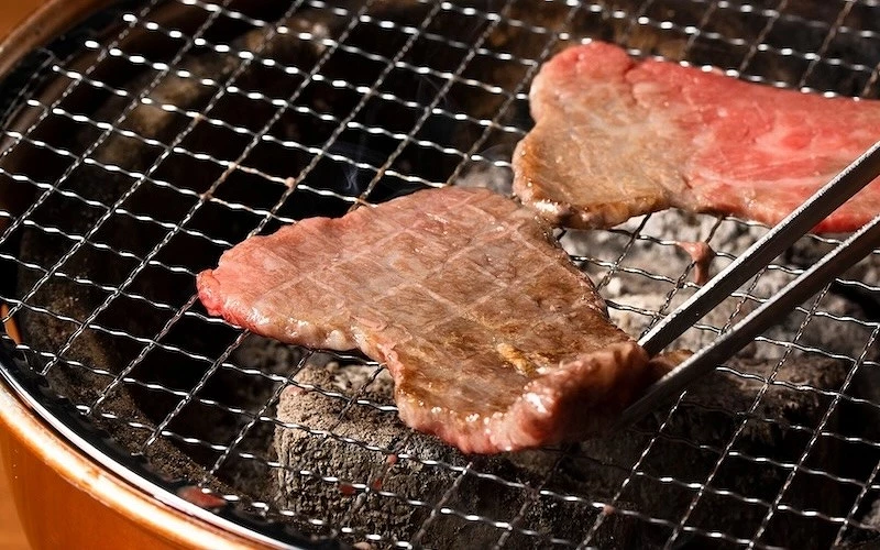 炭火烤爐上用夾子翻動兩片半熟和牛肉片