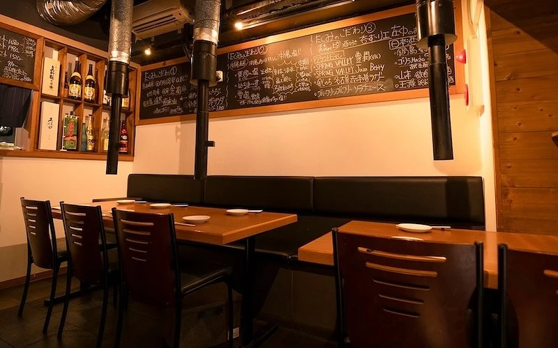 燒肉店內部，黑板上密寫日文菜單，沙發座與木桌排列整齊，牆邊陳列酒瓶