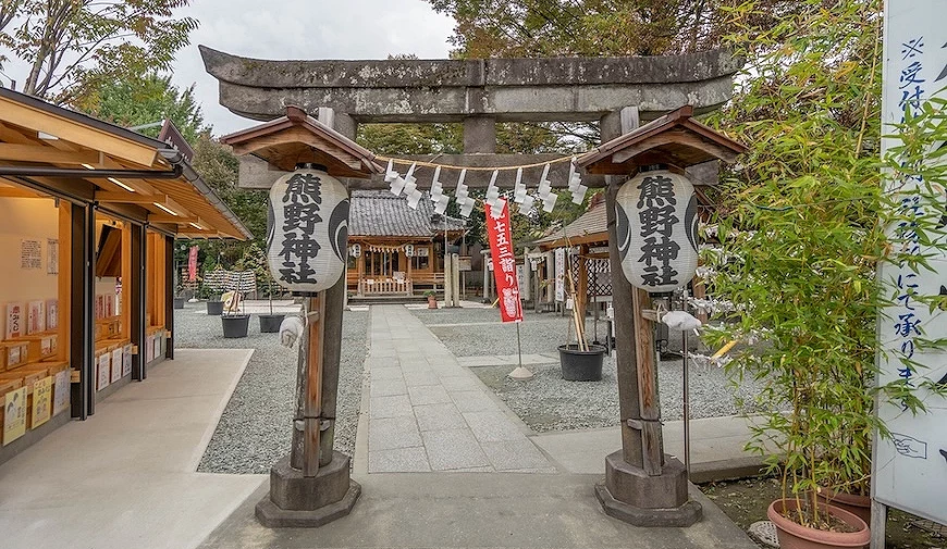 熊野神社鳥居入口,兩側立有寫著「熊野神社」的燈籠,正前方為社殿,掛有注連繩與紅色旗幟