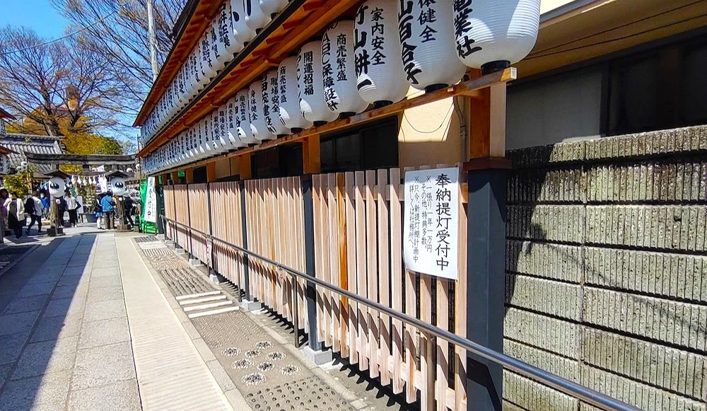日本神社境內走廊,掛有白色紙燈籠,柵欄上貼著「奉納提灯受付中」告示牌