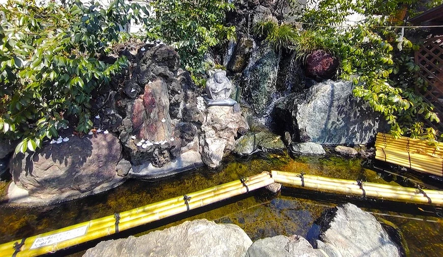 日式庭園石砌瀑布景觀,岩石中央置有石雕坐像,前方設竹製圍欄與淺水池