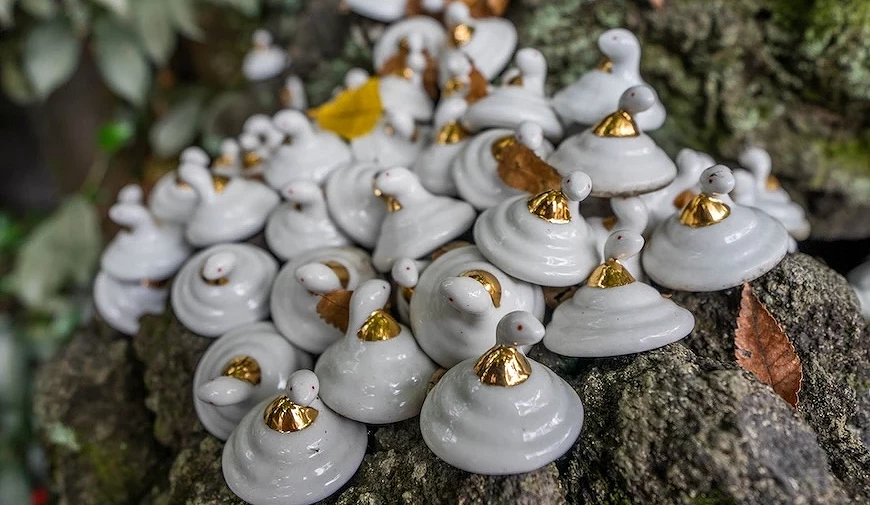 大量白色陶瓷蝸牛造型擺件,頂端附金色裝飾,密集陳列於岩石上