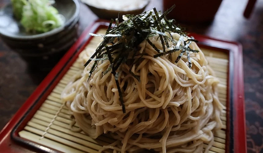紅色漆盤盛裝蕎麥冷麵,黑色海苔絲與白蔥段點綴,陶碗盛白色醬汁與綠芥末,日式蕎麥麵精緻誘人。