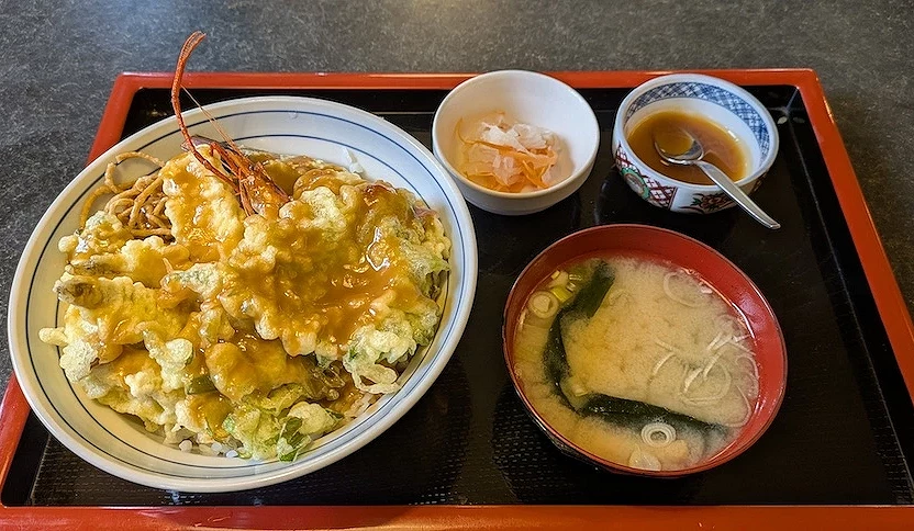 紅色漆盤盛裝日式定食,白瓷碗盛金黃蛋蓋飯與蝦,紅褐色味噌湯含海帶,白色陶碗盛湯品與配菜,銀色湯匙與調味醬,日本天婦羅蓋飯定食精緻美味。