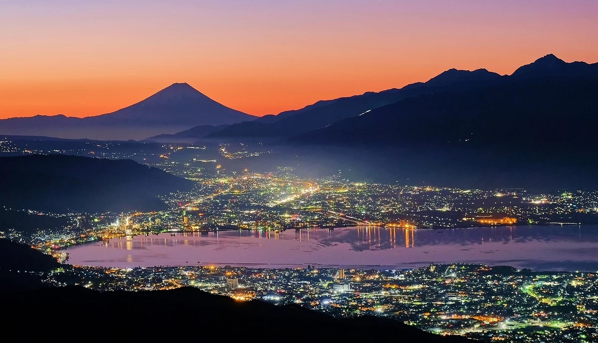 諏訪湖的夕照,湖邊燈火通明,遠處可見富士山
