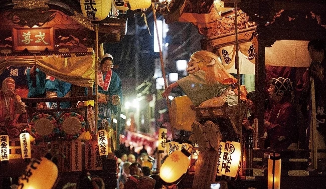 縣川越祭(川越まつり)夜間傳統曳山山車交會對演「曳っ合せ」場面,山車上掛滿點亮的燈籠與面具表演者