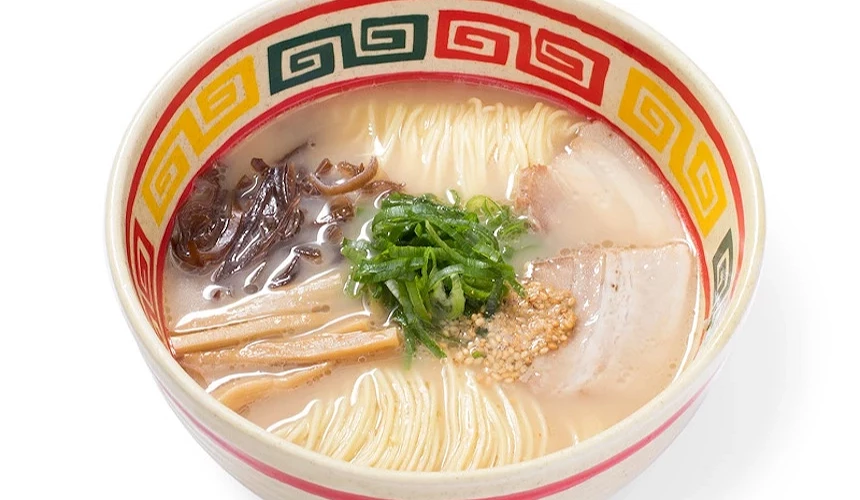紅白陶碗盛裝豚骨拉麵,黃色捲麵與豚肉片擺放,綠蔥與芝麻點綴,日式經典湯麵精緻。