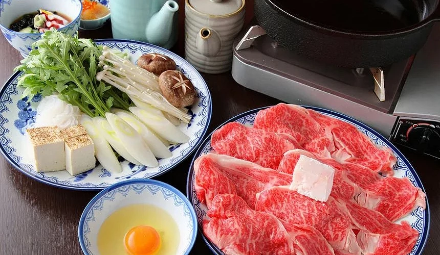 壽喜燒套餐。有一盤蔬菜和豆腐、一盤牛肉和一碗生雞蛋。